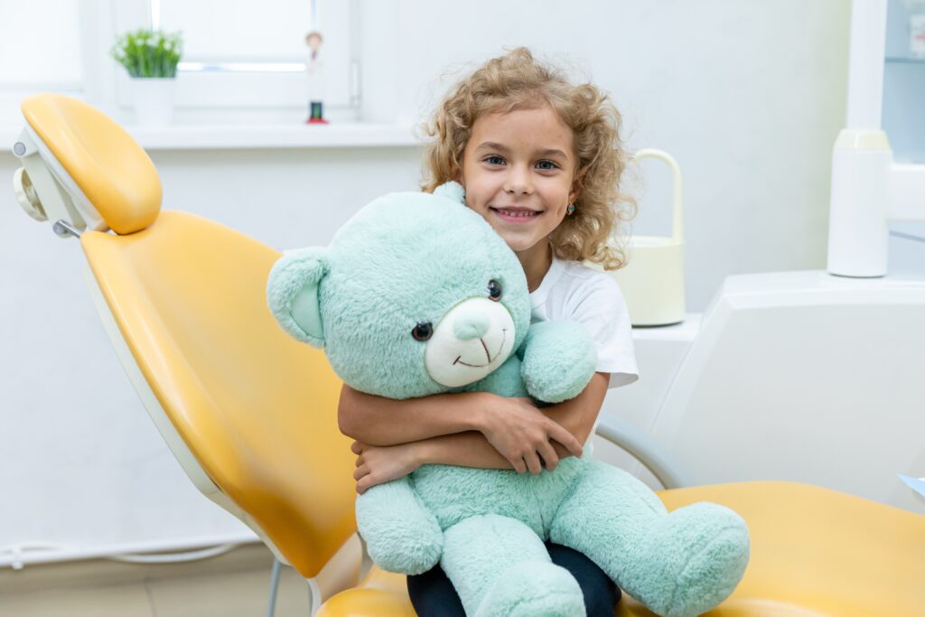 little girl hugging mint green teddy bear at dentist office