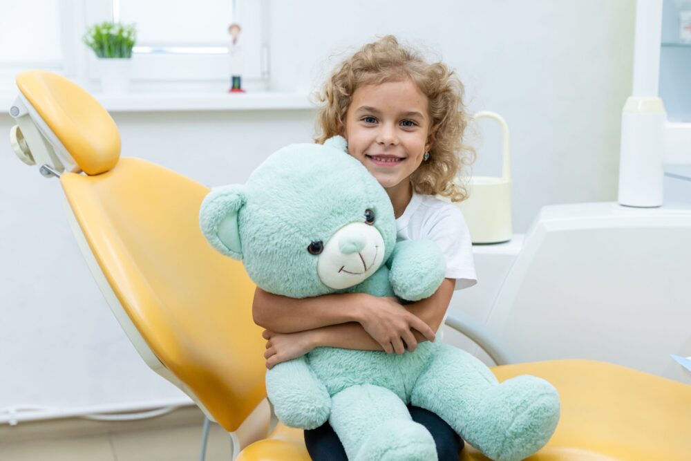 little girl hugging mint green teddy bear at dentist office